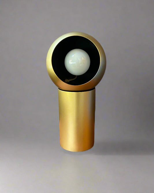 Gold cylindrical object with a white sphere inside on a wooden surface